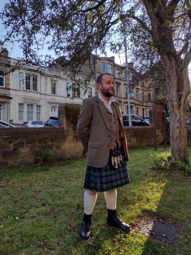 Me in a green tweed jacket, tweed waistcoat and a green kilt. I'm a beardy fool with short hair who is looking a bit smug.